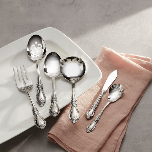 Silver cutlery set on a white plate with a pink napkin on a gray surface