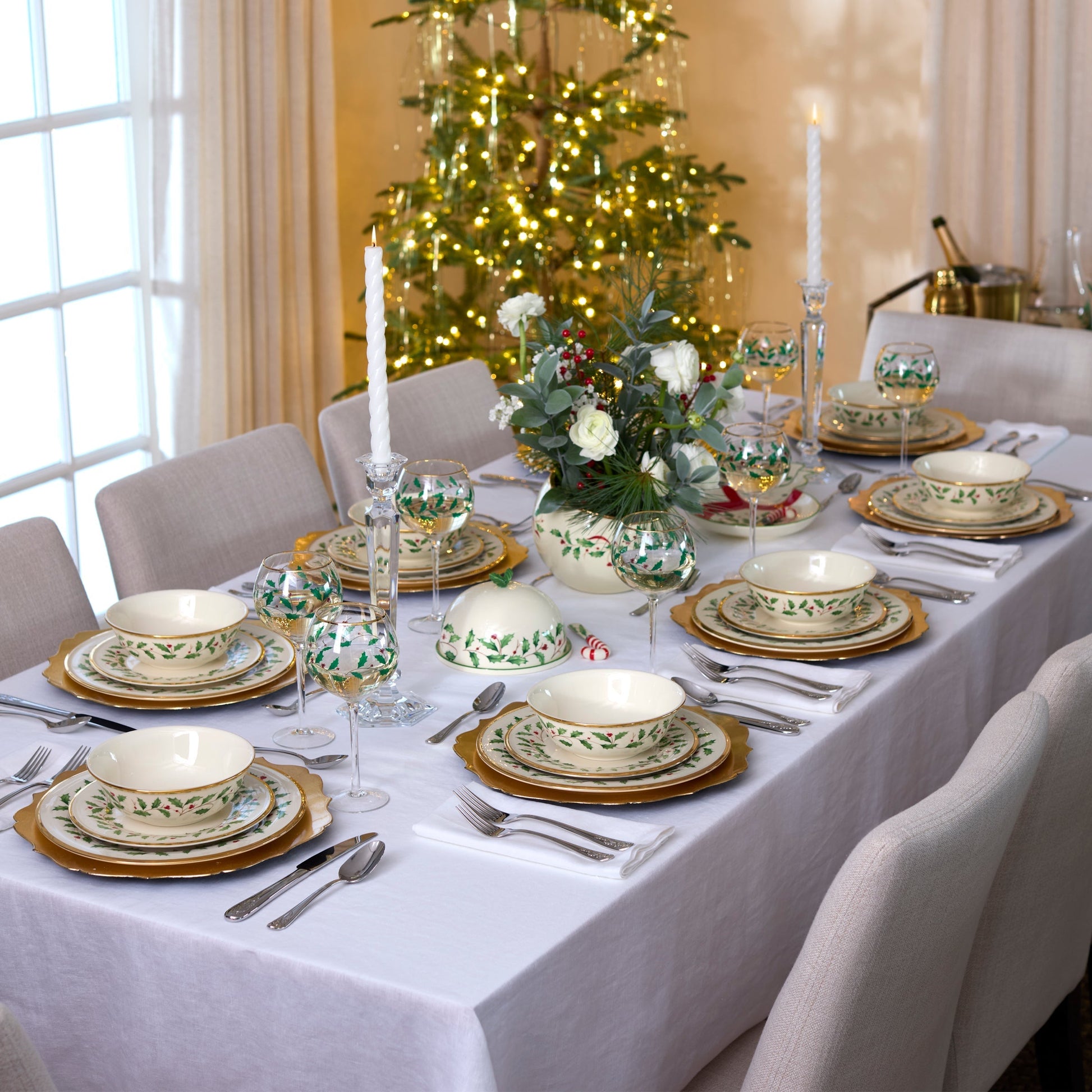 Elegant Christmas dinner table setting with floral centerpieces and a decorated tree in the background.