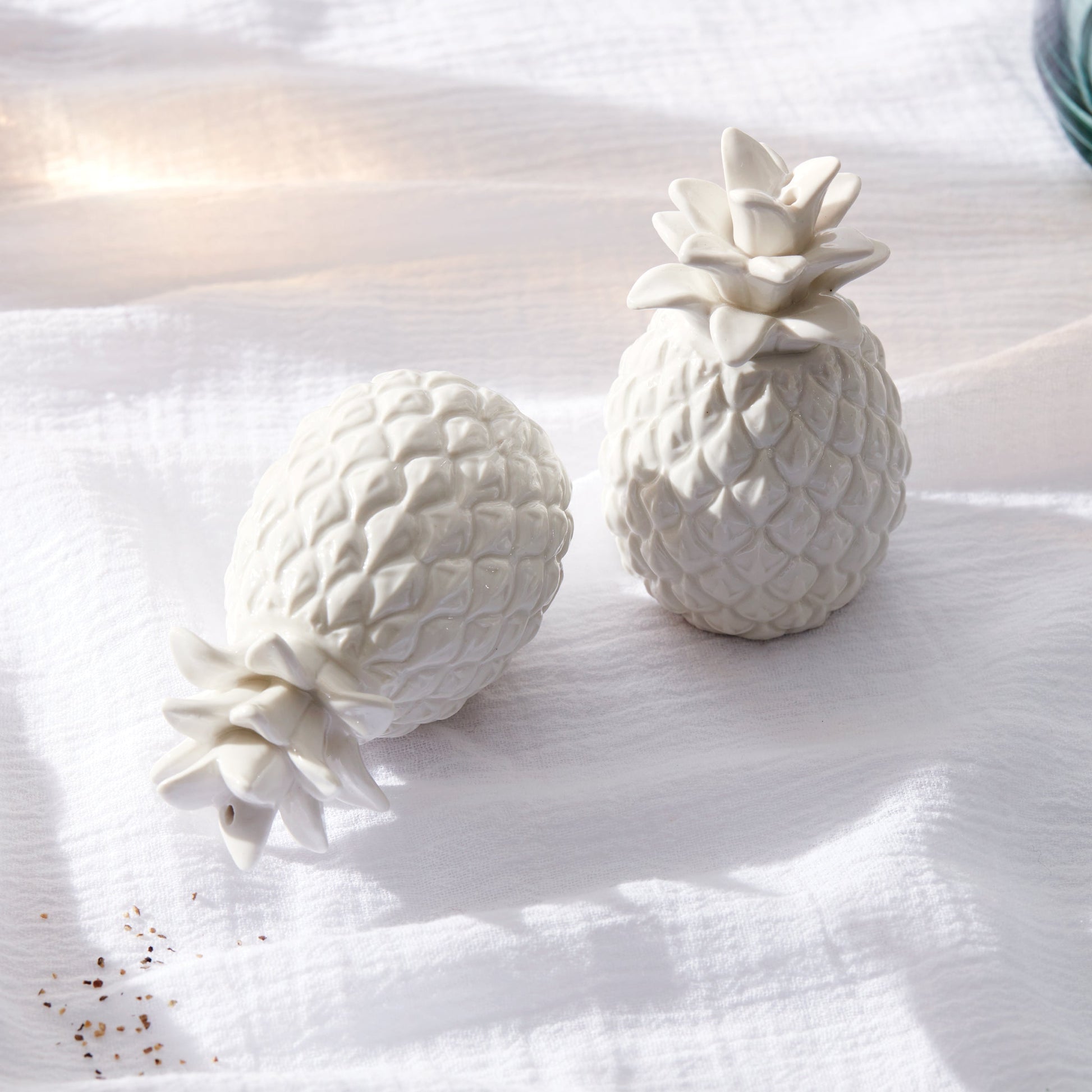 Two white ceramic pineapples on a textured surface with soft lighting.
