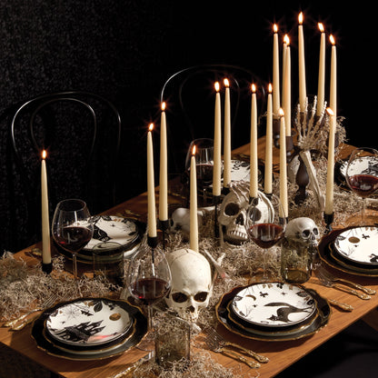 Halloween-themed table setting with skull decorations, candles, and black and white plates.